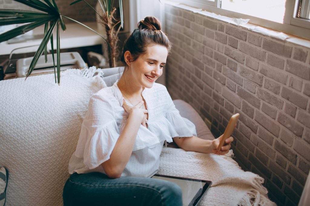 Happy woman enjoying a video call on her smartphone while sitting on a cozy sofa indoors.